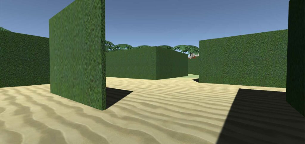 A virtual environment resembling a maze made of green hedges. The ground appears sandy, and the clear blue sky indicates it is daytime. The hedges are tall and create pathways forming a maze, with some trees visible above the hedges in the background.