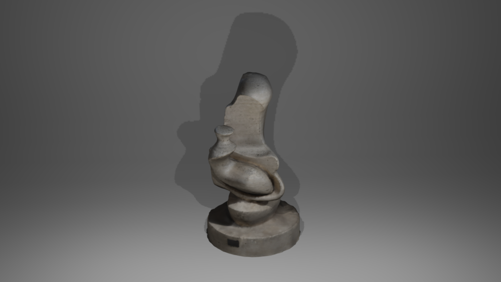 An abstract sculpture with an organic, flowing form made of a smooth, stone-like material. The sculpture is mounted on a round base and features curves and rounded shapes that suggest a modern or contemporary style. The central element is tall with a smaller, rounded protrusion near its base. The lighting creates a shadow behind the sculpture, adding depth to the image